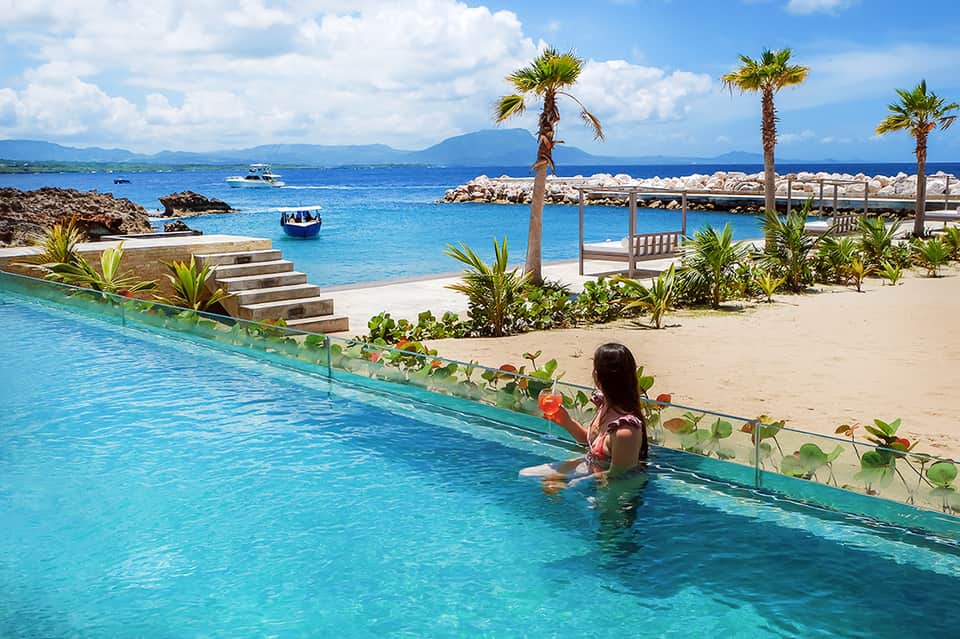 Infinity pool overlooking tropical beach with palm trees and crystal-clear turquoise water