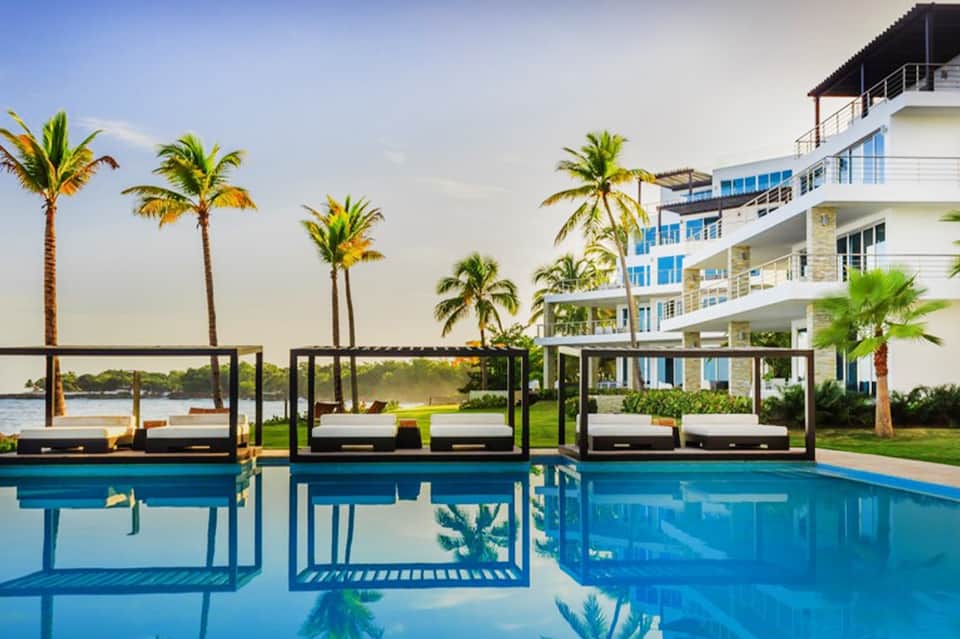 Luxury waterfront resort with palm trees, pool, lounge beds, and modern architecture