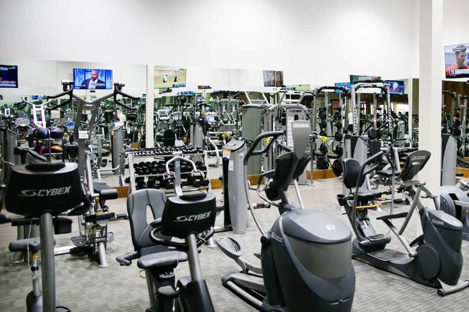 Modern fitness center with rows of Cybex exercise equipment and TV monitors on white walls