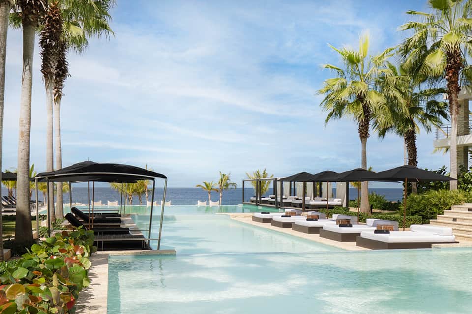 Luxurious oceanfront pool with black cabanas and palm trees at sunset