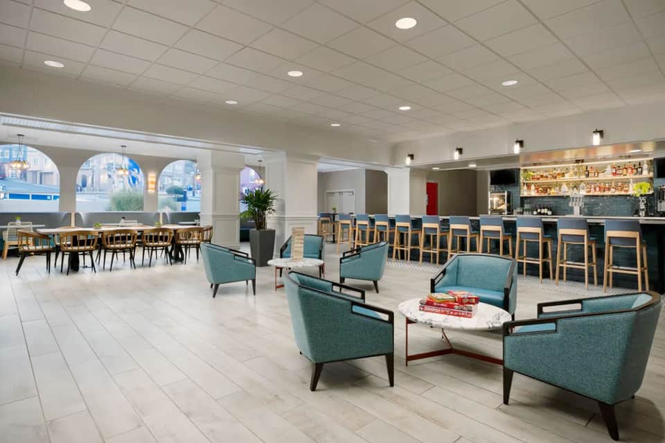 Spacious hotel lobby lounge with teal armchairs, bar seating, and arched windows