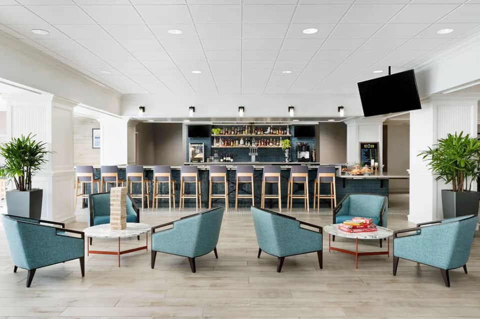 Modern hotel lobby and bar with turquoise chairs, wood flooring, and plants
