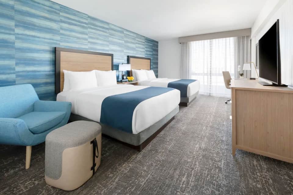 Modern hotel room with two queen beds, blue accent wall, and contemporary furnishings