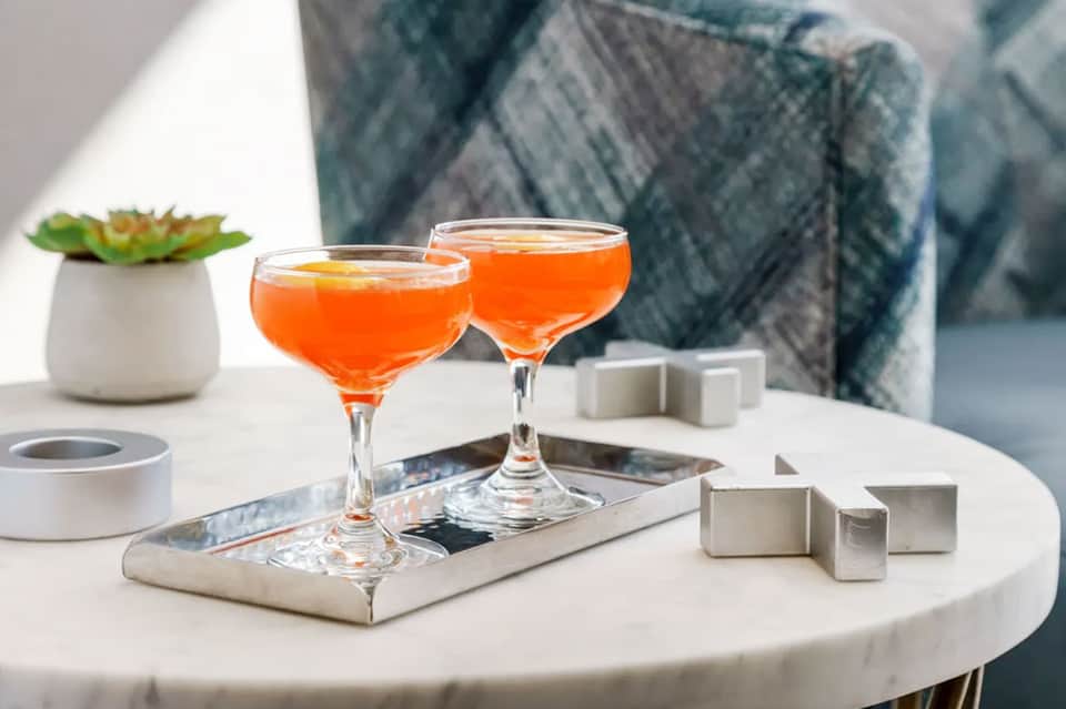 Two orange cocktails on white table with small succulent plant and decorative items