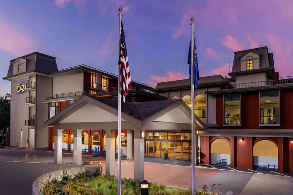 Modern resort building with mansard roof, red brick accents, white columns, illuminated at dusk with flags flying