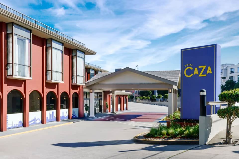 Hotel Caza entrance exterior with red colonnade architecture and blue signage on sunny day