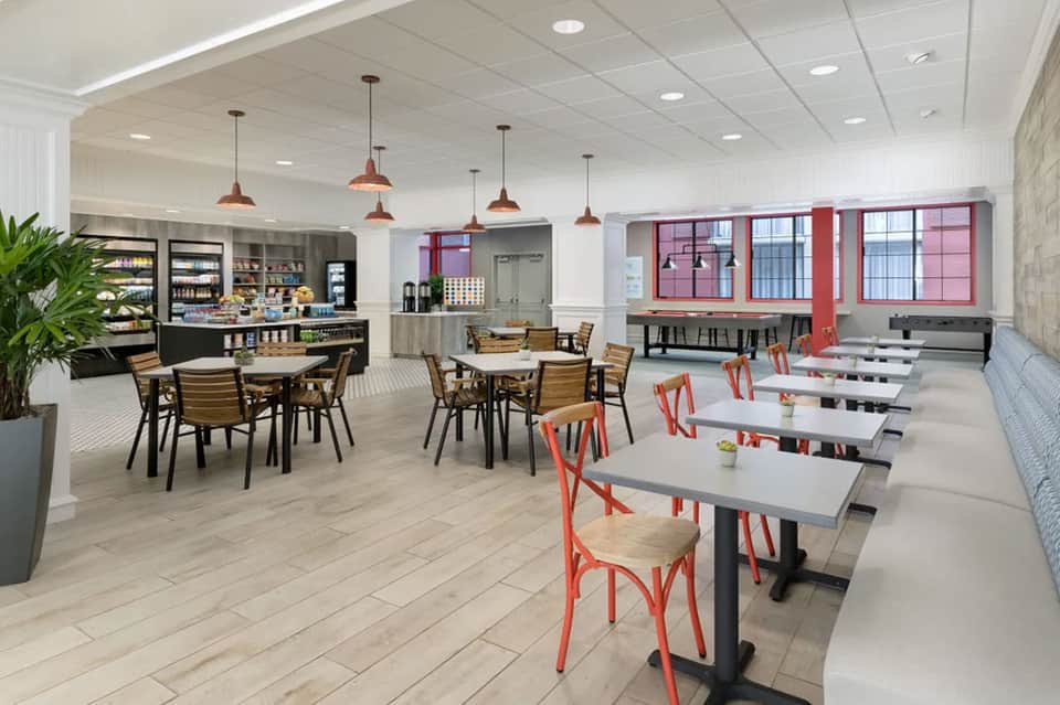 Hotel cafe with dining tables, red chairs, counter service area, and large windows