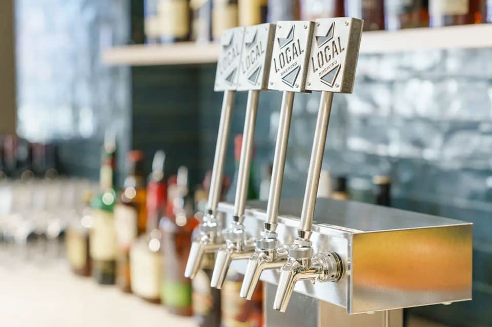 Multiple beer tap handles labeled 'Local' at a bar counter with bottles displayed in background