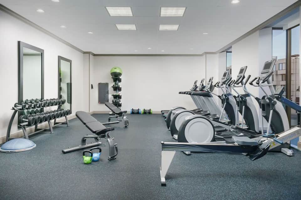 Fitness center with cardio equipment, free weights, mirrors, and bright natural lighting from windows