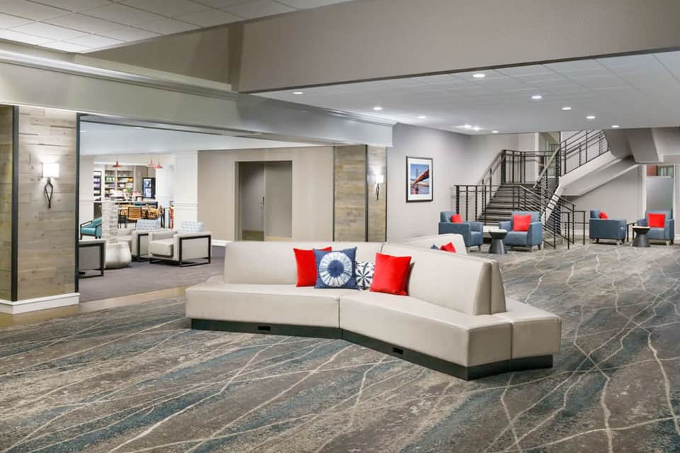 Modern hotel lobby with curved white seating, stairs, and colorful accent pillows