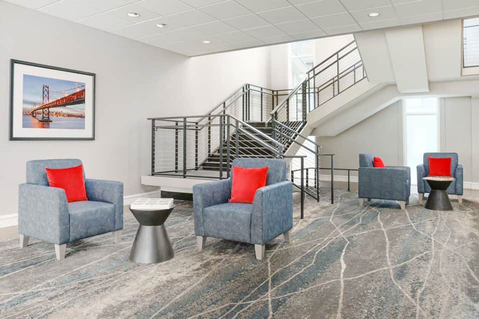 Contemporary lobby lounge with blue armchairs, red pillows, modern staircase, and clean design