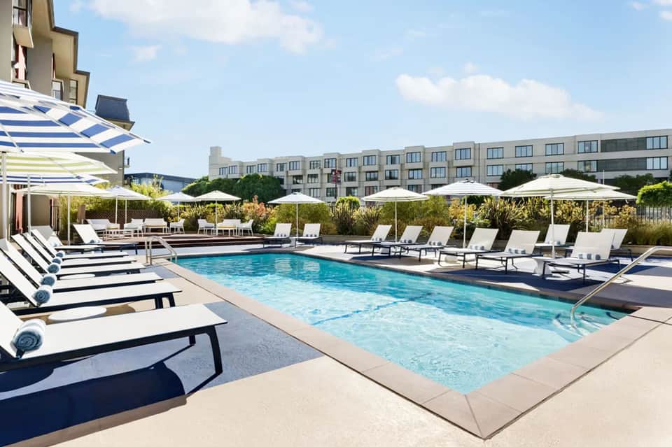 Contemporary pool deck with blue and white striped loungers, umbrellas, modern hotel building, and landscaping