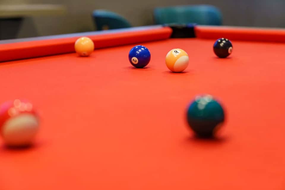 Billiards game setup on bright orange pool table with colorful numbered balls in resort recreation area