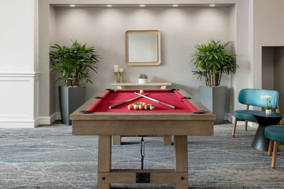 Elegant billiards room with red felt pool table, decorative plants, and contemporary furnishings