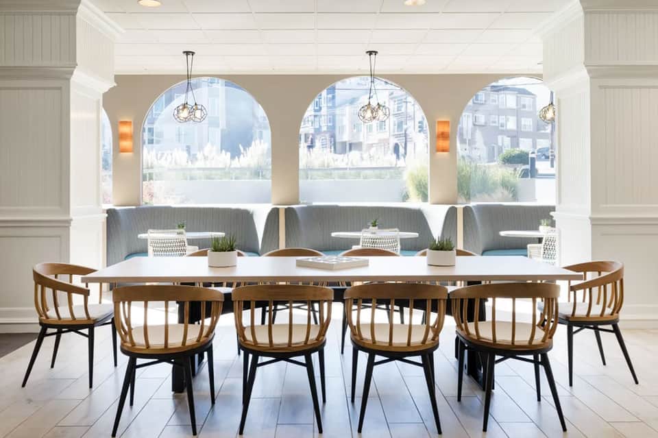 Bright dining room with wooden chairs, long white table, arched windows, and waterfront views