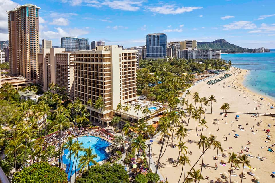 Aerial view of beachfront resort with pools, palm trees, sandy beach, and turquoise ocean waters