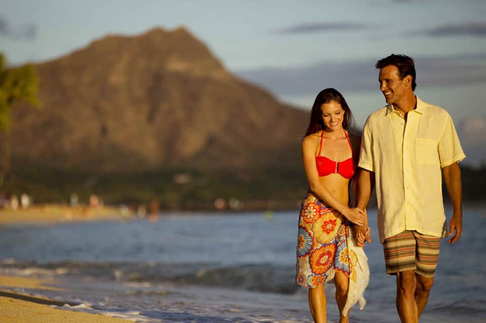 Couple walking on beach holding hands with mountain backdrop and calm ocean waters