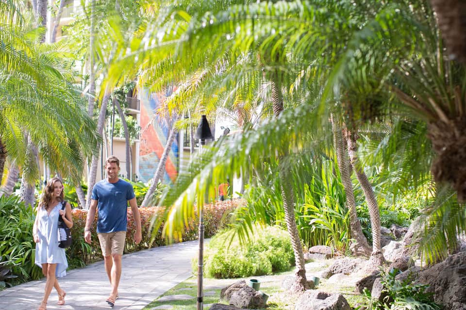 Couple walking through palm tree-lined tropical pathways at resort grounds