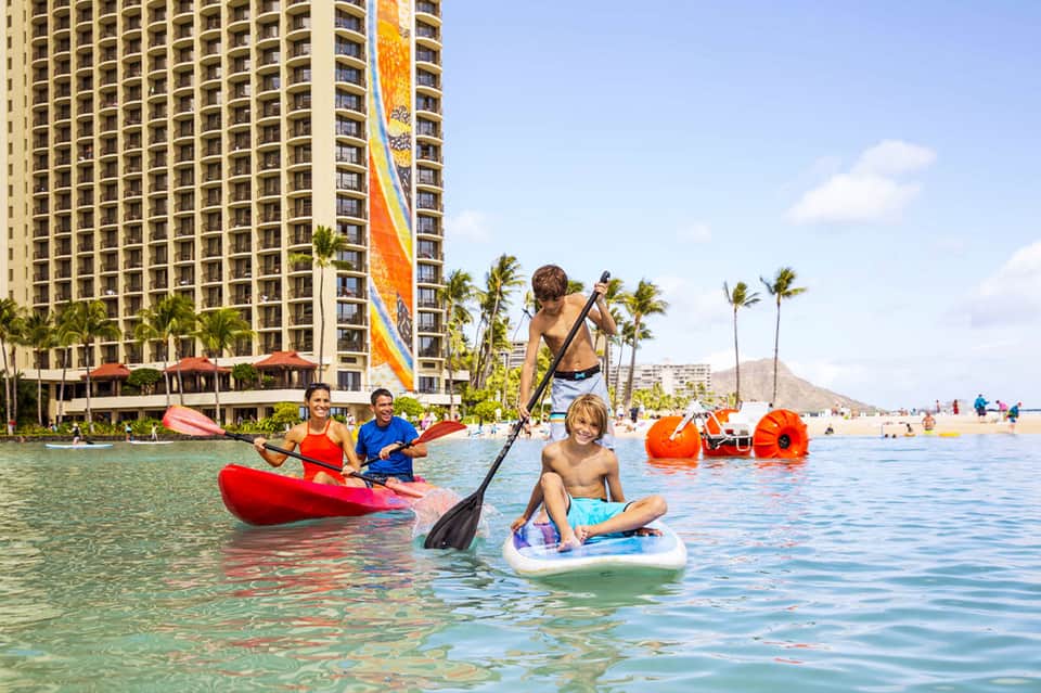 Beachfront resort tower with water sports activities including paddleboards and kayaks in shallow turquoise water