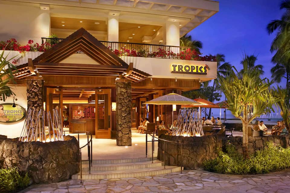 Tropics restaurant entrance at dusk with stone accents, palm trees, and oceanfront terrace