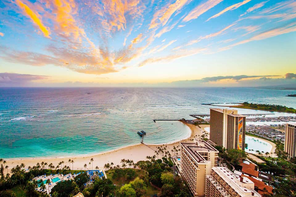 Sunset over ocean beach with high-rise resort buildings and palm trees on sandy shore