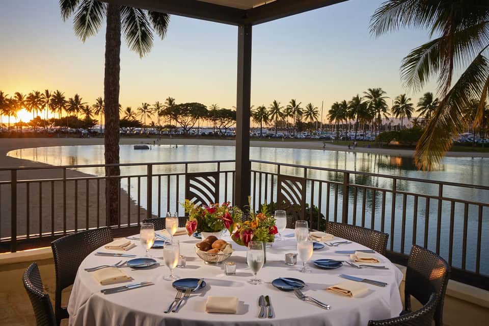 Fine dining table set for four overlooking waterway at sunset with palm trees and boats