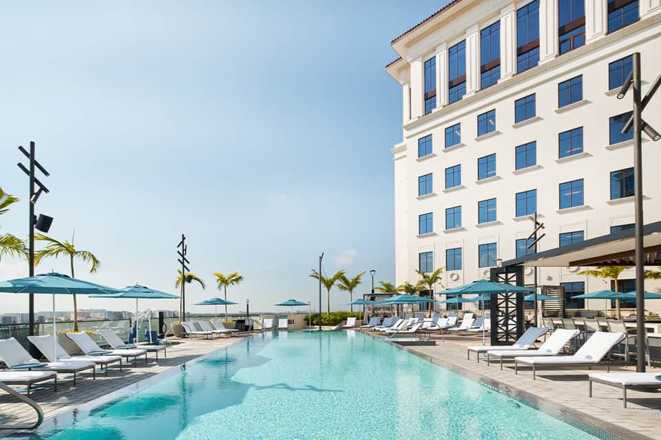 Resort infinity pool overlooking city skyline with white hotel building and palm trees