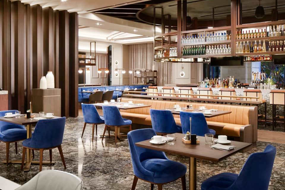 Modern restaurant interior with blue velvet chairs, wooden booths, and illuminated bar