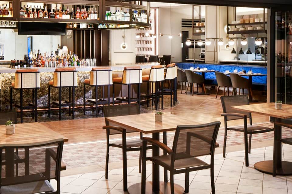 Modern hotel bar and restaurant with wooden tables, blue accent wall, and stocked shelves