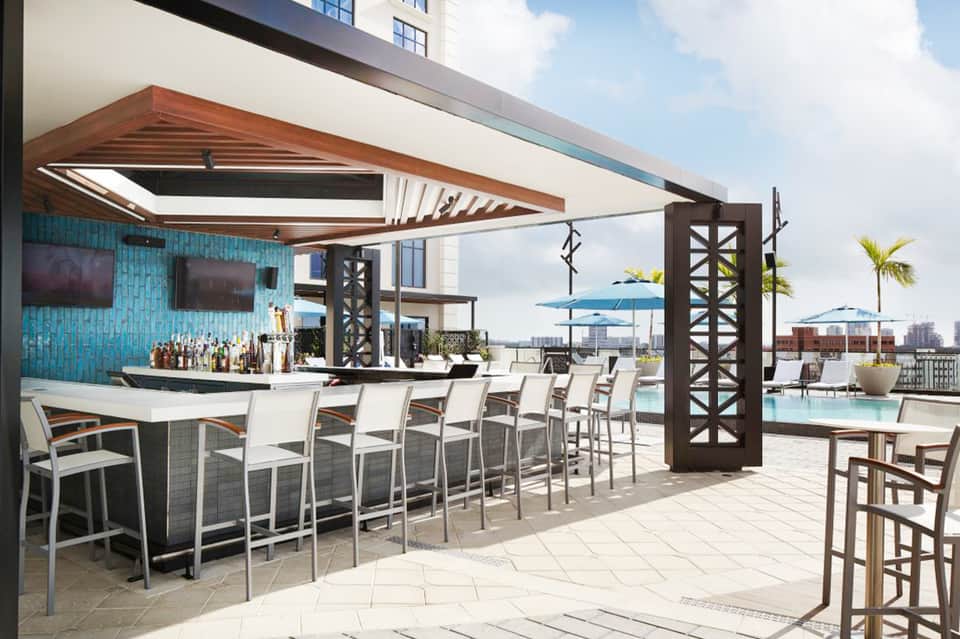 Upscale rooftop bar with turquoise tile, wooden shade structure, and city skyline