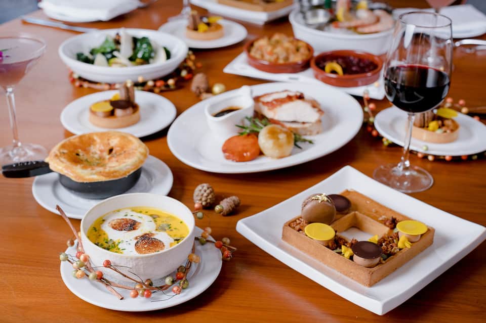 Fine dining spread with multiple plated dishes, salads, and wine on wooden table