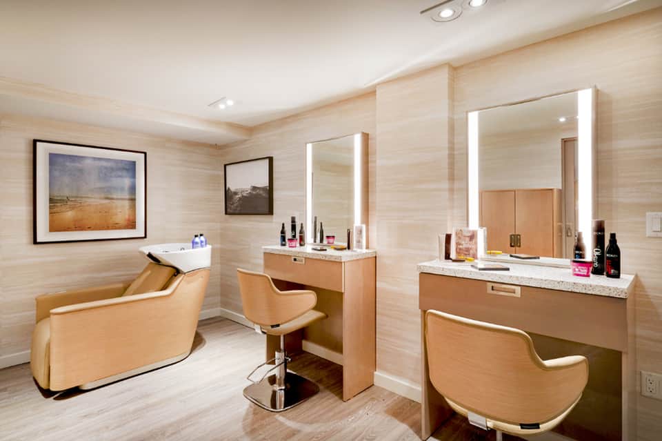 Luxury spa room with dual vanities, illuminated mirrors, and upholstered seating