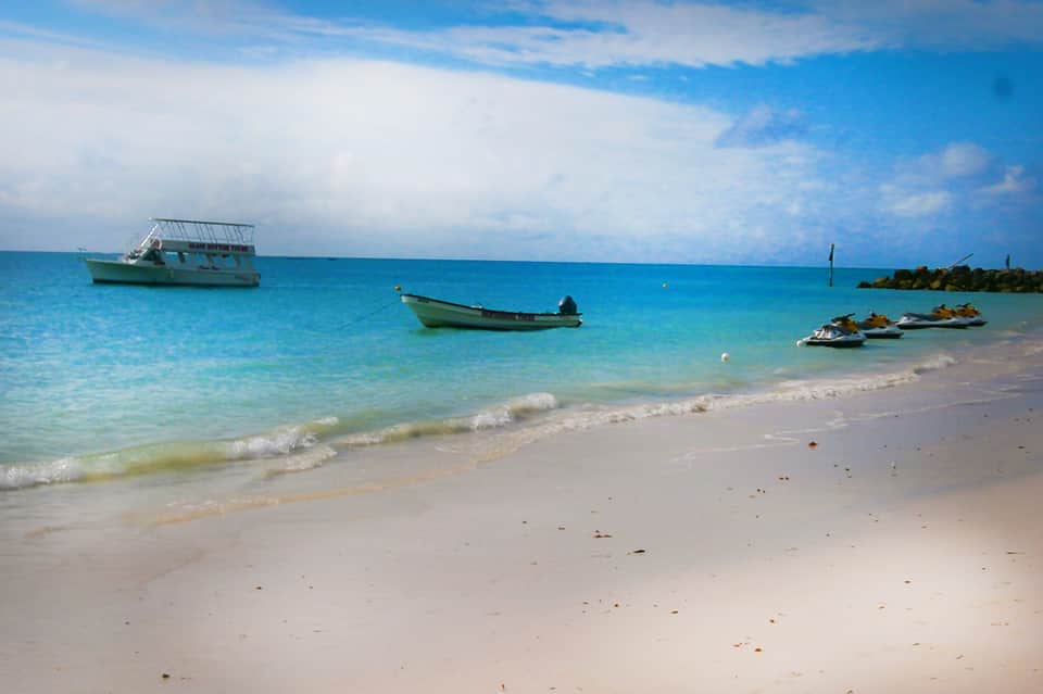 Tropical beach with turquoise water, white sand, and fishing boats anchored offshore