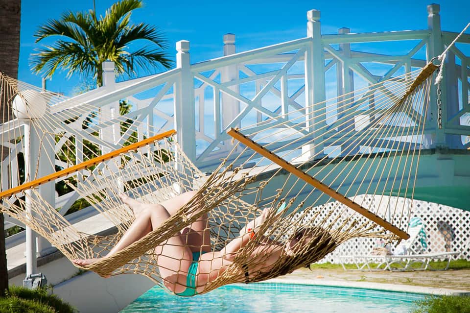 Woman relaxing in woven hammock overlooking ocean with white railing and palm trees