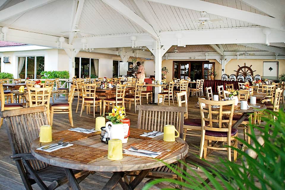 Covered outdoor dining terrace with wooden tables, wicker chairs, and nautical décor elements