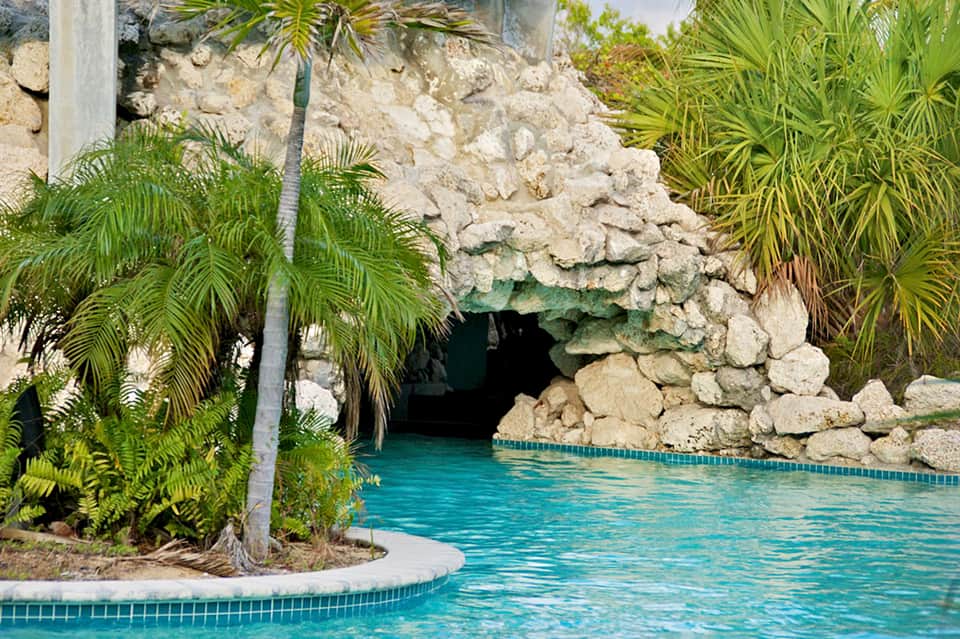 Turquoise cave pool entrance surrounded by limestone rocks and tropical plants