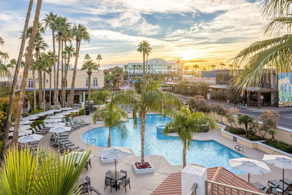 Aerial view of sprawling resort pool complex with palm trees at sunset with mountain backdrop