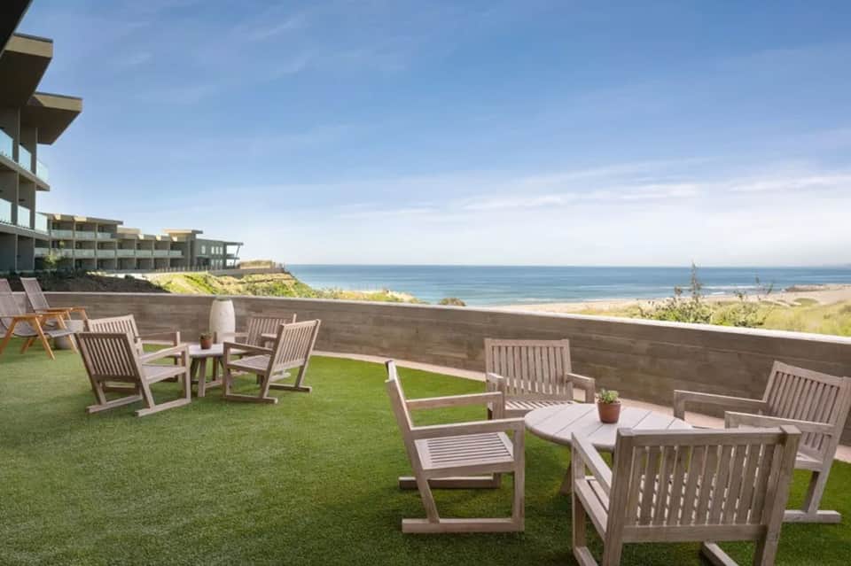 Oceanfront terrace with wooden lounge chairs overlooking beach, modern hotel building, and coastal landscape