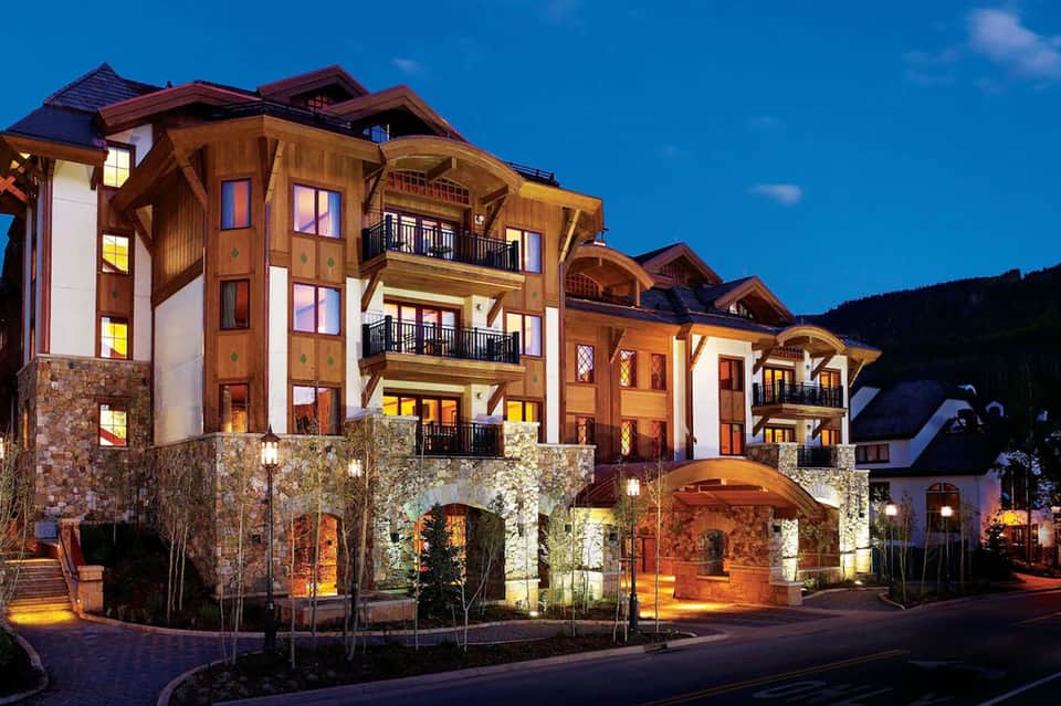 Luxury mountain resort building illuminated at dusk with stone and timber architecture and manicured landscaping