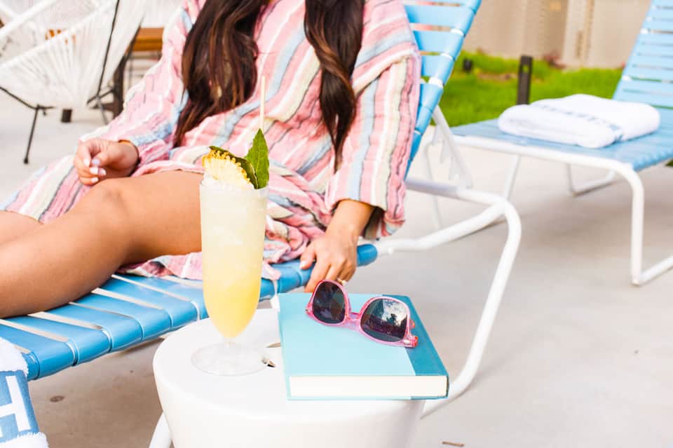 Woman in striped shirt relaxing on blue lounge chair with yellow cocktail and pink sunglasses
