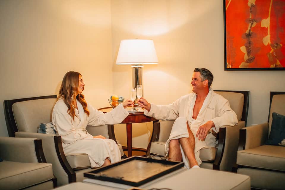 Couple toasting drinks in spa robes in elegant hotel lounge with warm lighting