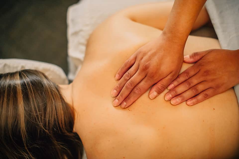 Therapist performing back massage on woman lying on massage table