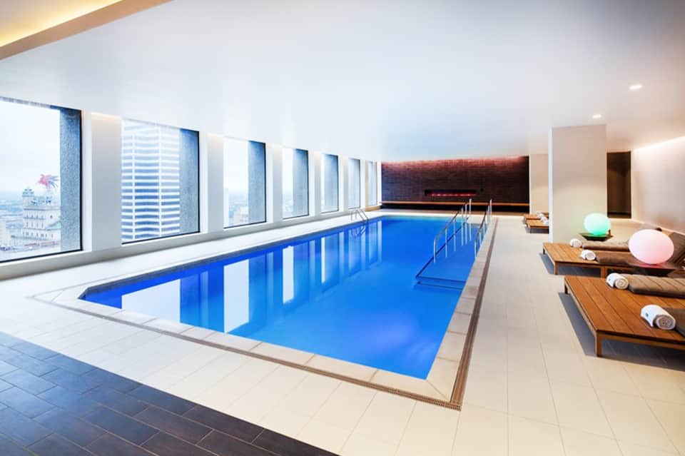 Indoor lap pool with large windows overlooking city skyline and relaxation area