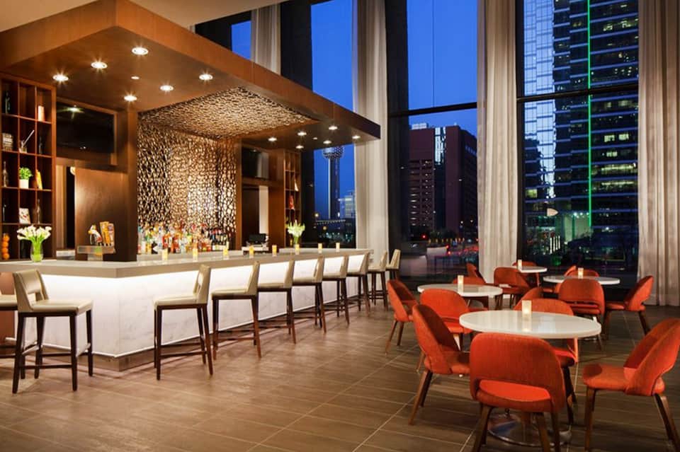 Upscale lounge with wood bar, orange seating, and cityscape view at night