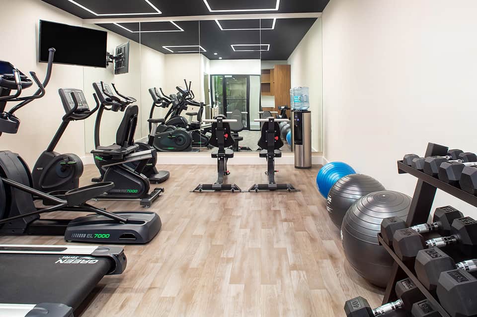 Modern resort fitness center with exercise bikes, ellipticals, weights, and mirrors