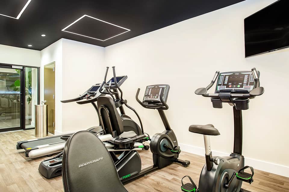 Hotel fitness center with cardio equipment, treadmills, and modern LED ceiling lights