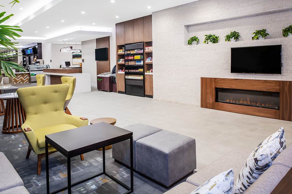 Modern hotel lobby with yellow accent chair, fireplace, wood paneling, and contemporary furnishings