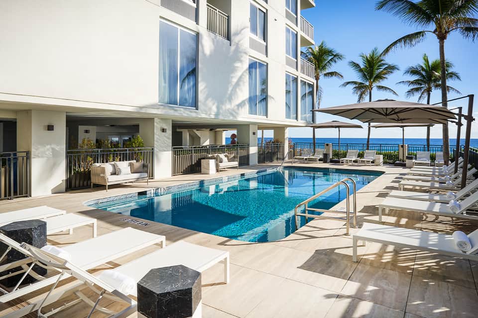 Oceanfront pool deck with lounge chairs, umbrellas, and beachfront condominium building