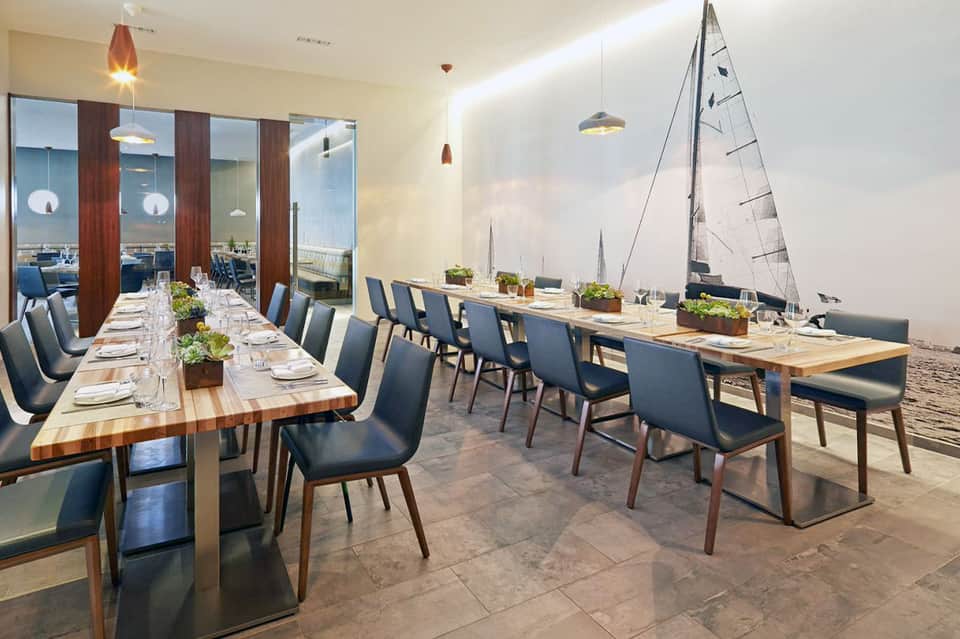 Elegant dining room with long wooden tables, blue chairs, and sailing boat artwork on walls