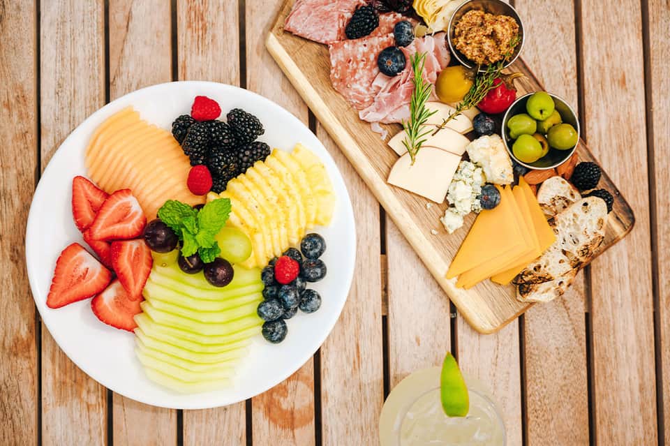 Overhead view of fruit and charcuterie board with cheese, meats, berries on wooden deck